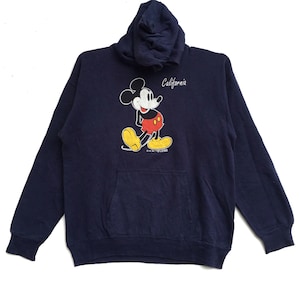 K&ouml;nnte beinhalten: Ein marineblauer Kapuzenpullover mit einem Mickey-Mouse-Motiv und dem Schriftzug "California" auf der Vorderseite.