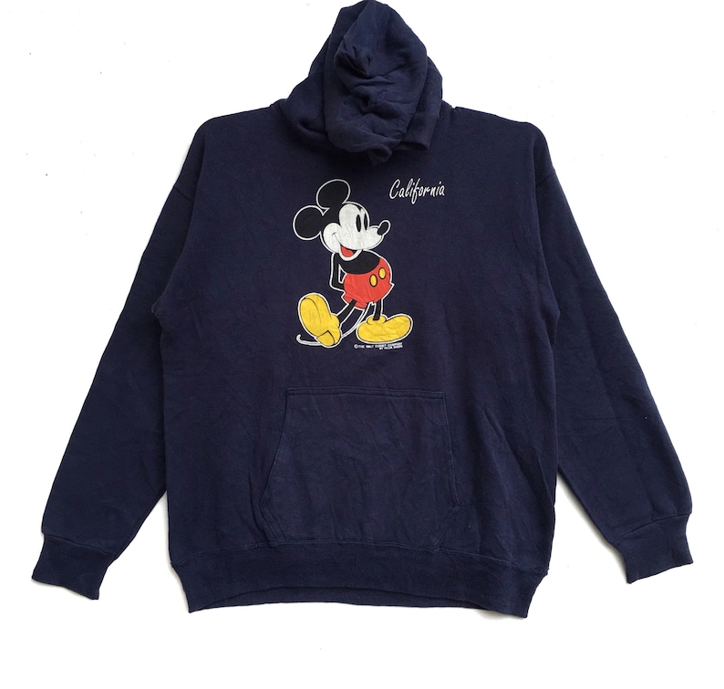 K&ouml;nnte beinhalten: Ein marineblauer Kapuzenpullover mit einem Mickey-Mouse-Motiv und dem Schriftzug "California" auf der Vorderseite.
