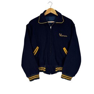 May include: A navy blue varsity jacket with yellow accents. The jacket features a yellow collar, pocket trim, and striped cuffs and hem. The name "Warren" is embroidered in yellow script on the chest. The jacket is hanging on a wooden hanger.