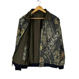 May include: A green, brown and black camouflage jacket with a zip closure. The jacket has a black collar and a black waistband.