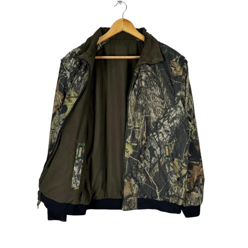 May include: A green, brown and black camouflage jacket with a zip closure. The jacket has a black collar and a black waistband.
