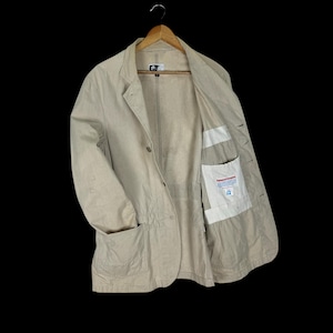 Puede incluir: Una chaqueta de lino beige con cierre de botones y un bolsillo de parche en el lado izquierdo. La chaqueta tiene un forro blanco y una etiqueta que dice "International Exclusive".
