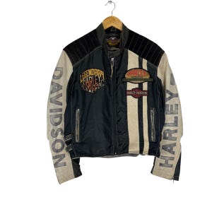May include: Black and tan Harley-Davidson motorcycle jacket with the words "DAVIDSON" and "HARLEY" printed on the sleeves. The jacket has a zipper closure and multiple patches with the Harley-Davidson logo.