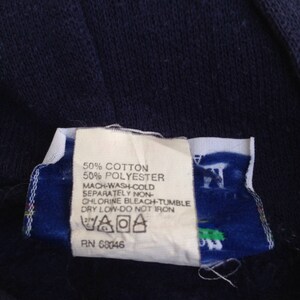 K&ouml;nnte beinhalten: Ein wei&szlig;es Pflegeetikett mit schwarzem Text, der "50% Baumwolle 50% Polyester Maschinenw&auml;sche kalt Separat Nicht-Chlorbleiche - Trocknergeeignet bei niedriger Temperatur - Nicht b&uuml;geln" und eine Pflege-Symbolgrafik lautet. Das Etikett tr&auml;gt auch den Text "PN 68046".