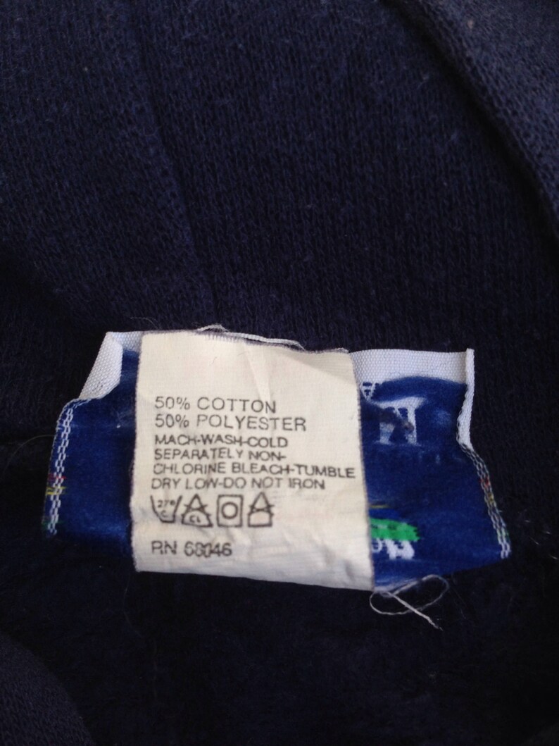 K&ouml;nnte beinhalten: Ein wei&szlig;es Pflegeetikett mit schwarzem Text, der "50% Baumwolle 50% Polyester Maschinenw&auml;sche kalt Separat Nicht-Chlorbleiche - Trocknergeeignet bei niedriger Temperatur - Nicht b&uuml;geln" und eine Pflege-Symbolgrafik lautet. Das Etikett tr&auml;gt auch den Text "PN 68046".