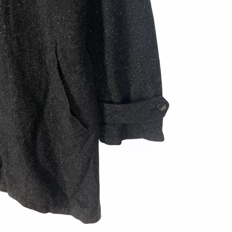 May include: A dark gray tweed coat with a button on the cuff. The coat has a textured fabric and a relaxed fit.