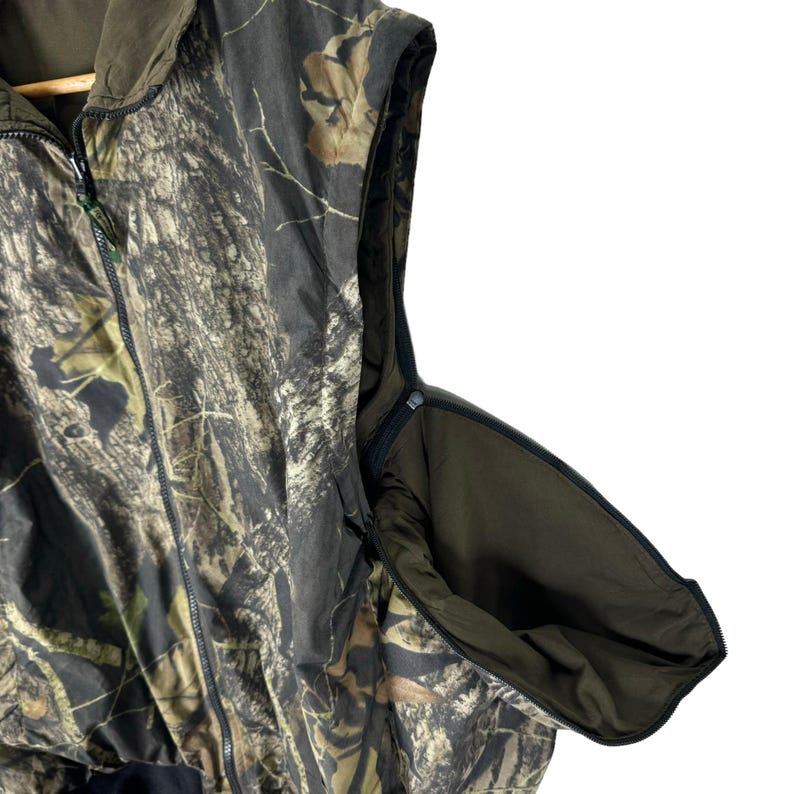 May include: A sleeveless camouflage hunting vest with a zip closure and a hood. The vest has a large pocket on the side.