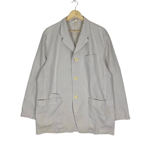 May include: A light grey linen blazer with three buttons and two large pockets.