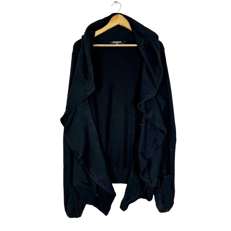 May include: Black hooded cardigan with a ruffled front and a long, asymmetrical hem. The cardigan is made of a soft, comfortable fabric and has a relaxed fit.