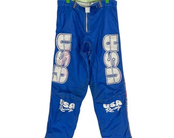 Könnte beinhalten: Blaue Skihose mit weißen "USA Racing" und "CSE" Logos an den Seiten. Die Hose hat einen roten und weißen Streifen an den Seitennähten.