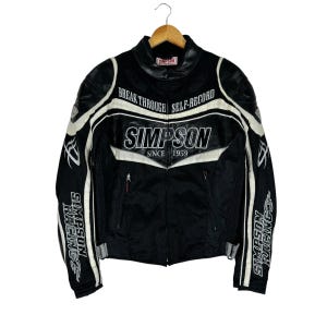 May include: Black leather motorcycle jacket with white accents. The jacket has the text "Simpson Racing" on the sleeves and "Simpson Since 1959" on the chest. The jacket also has the text "Break Through Self-Record" on the chest.