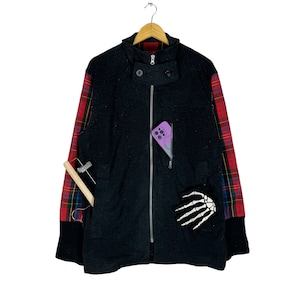 Pode incluir: Uma jaqueta preta com zíper com forro xadrez vermelho e preto. A jaqueta tem um bolso com zíper no lado esquerdo e um patch de mão de esqueleto no lado direito.