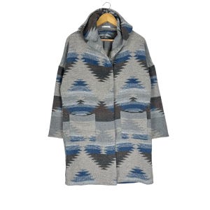 Può includere: Una tazza di ceramica bianca con manico nero e la scritta "But First, Coffee" in grassetto nero. La tazza è appoggiata su una superficie di legno. La tazza è alta circa 10 cm.