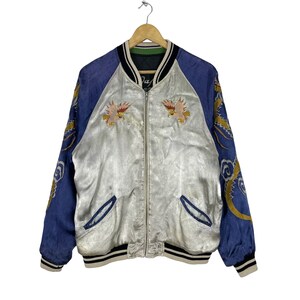May include: A silver satin bomber jacket with blue sleeves. The sleeves feature embroidered dragons and clouds. The jacket has a zipper closure and a ribbed collar, cuffs, and hem.