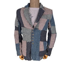 May include: A patchwork blazer in shades of blue, gray, and tan. The jacket features a mix of textured fabrics, a notched lapel, and four button closure. The blazer is displayed on a mannequin.
