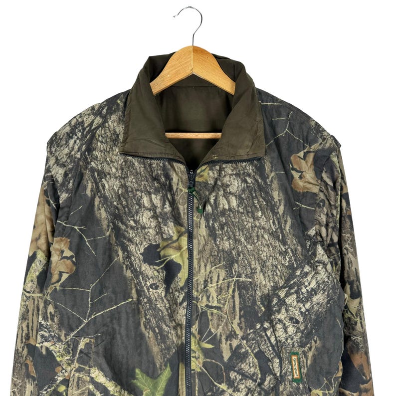 May include: A camouflage jacket with a zip fastening and a brown fleece lining. The jacket has a "Realtree" logo on the lower right side.
