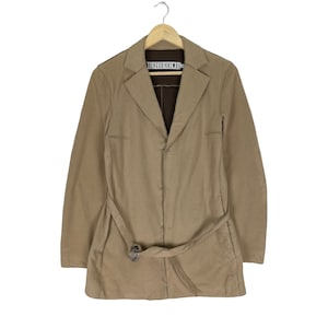 May include: A tan belted blazer with a single button closure and the text "BERGSBIKKEMBERGS" on the label.