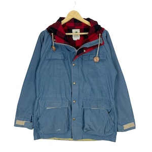 May include: A blue hooded jacket with a red and black plaid lining. The jacket has a zipper closure, multiple pockets, and a drawstring waist. The label on the jacket reads "Sierra Designs".