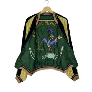 May include: A green and black reversible bomber jacket with a yellow and black striped trim. The inside of the jacket features an embroidered image of the Road Runner cartoon character with the text "Road Runner" above it.