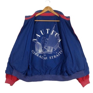 Puede incluir: Una chaqueta reversible azul y roja con un logotipo de Nautica y las palabras "Gibraltar Straits" impresas en la espalda.