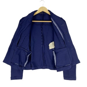 Puede incluir: Una chaqueta azul marino con cierre de botones y dos bolsillos. La chaqueta tiene una tela texturizada y una longitud ligeramente recortada.