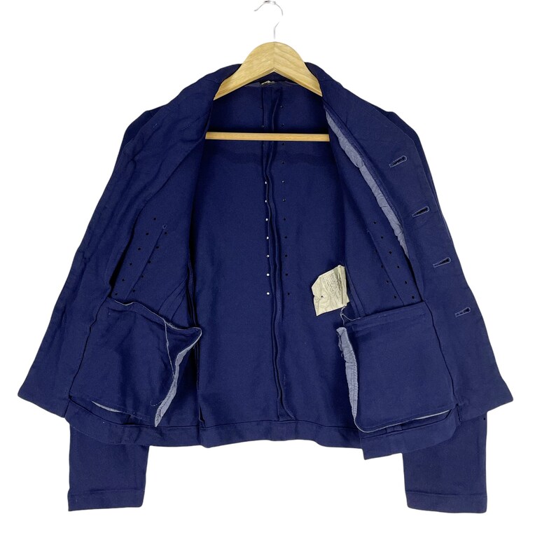 Puede incluir: Una chaqueta azul marino con cierre de botones y dos bolsillos. La chaqueta tiene una tela texturizada y una longitud ligeramente recortada.