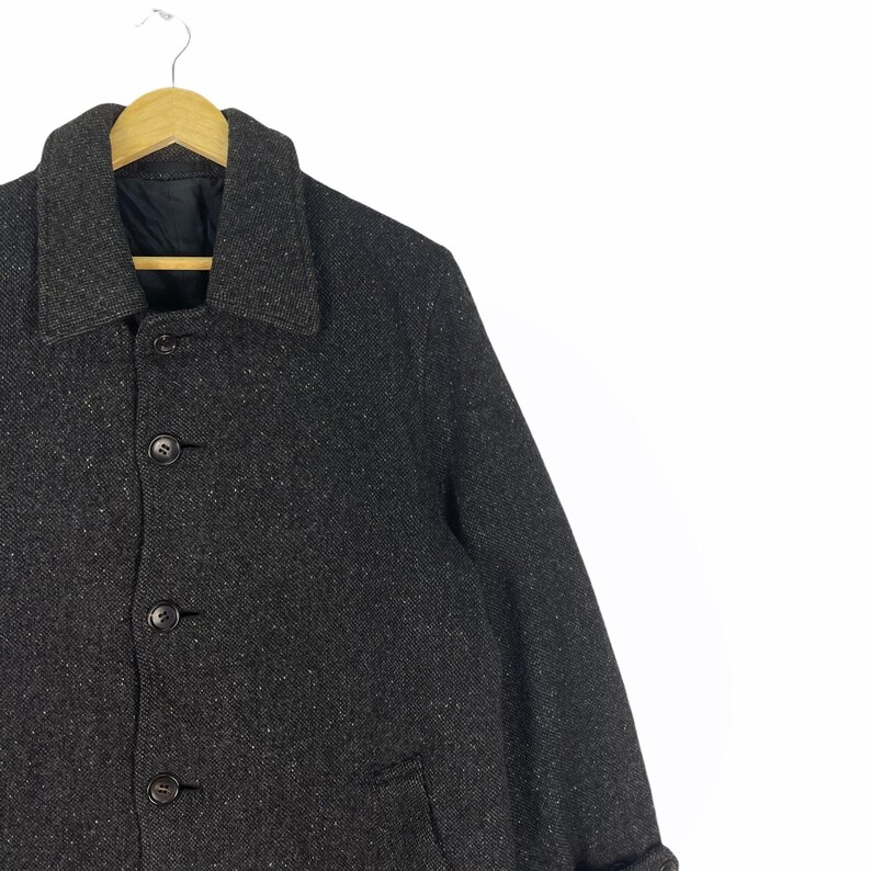 May include: A dark gray tweed jacket with a button-up front and a single pocket on the left side.