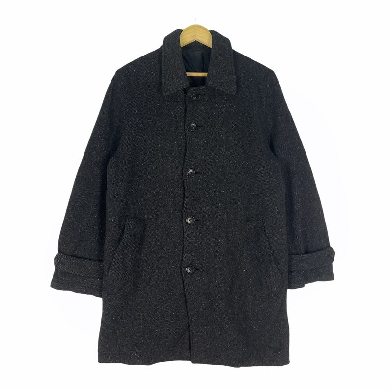 May include: A dark gray wool coat with a button closure and two pockets. The coat has a slightly textured surface and a collar.