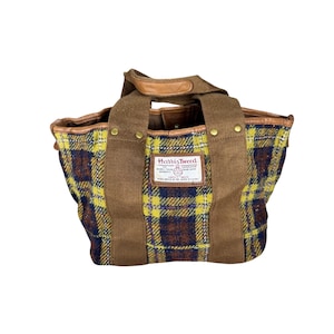 May include: A brown tote bag with a yellow and blue plaid pattern. The bag has brown leather handles and trim, and a label that reads "Harris Tweed". The bag is made of a sturdy fabric and has a classic design.