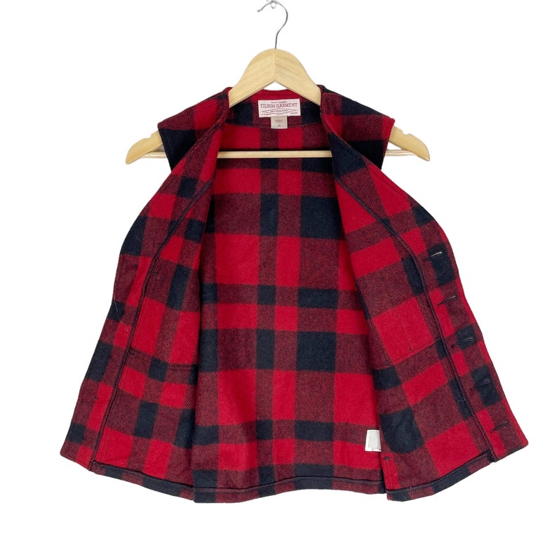 Op de afbeelding: Rood en zwart geruit flanellen vest met knoopsluiting. Het vest is gevoerd met een rood en zwart geruit stof. Het label op het vest luidt "Filson Garments".