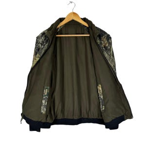 May include: A camouflage print jacket with a zip fastening and a black lining. The jacket is unbuttoned and hanging on a wooden hanger.