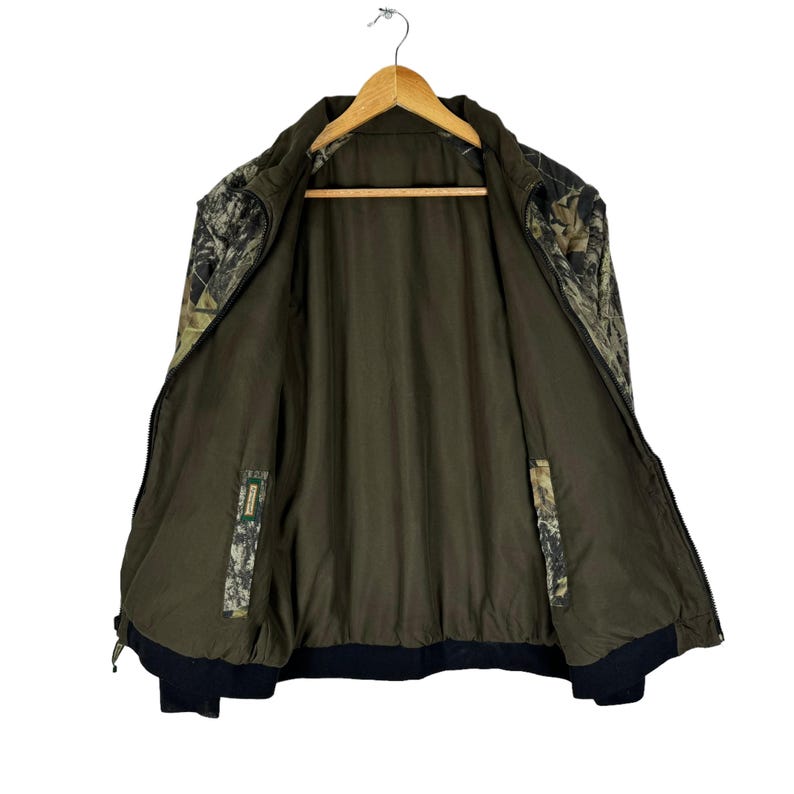 May include: A camouflage print jacket with a zip fastening and a black lining. The jacket is unbuttoned and hanging on a wooden hanger.