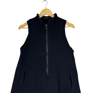 K&ouml;nnte beinhalten: Ein schwarzes, &auml;rmelloses Kleid mit einem Rei&szlig;verschluss vorne und zwei Taschen an den Seiten. Das Kleid ist aus einem strukturierten Stoff.