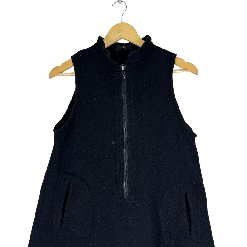 K&ouml;nnte beinhalten: Ein schwarzes, &auml;rmelloses Kleid mit einem Rei&szlig;verschluss vorne und zwei Taschen an den Seiten. Das Kleid ist aus einem strukturierten Stoff.