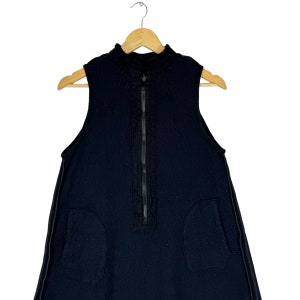 K&ouml;nnte beinhalten: Ein schwarzes, &auml;rmelloses Kleid mit einem Rei&szlig;verschluss an der Vorderseite und zwei Taschen an den Seiten. Das Kleid hat einen hohen Ausschnitt und eine lockere Passform.