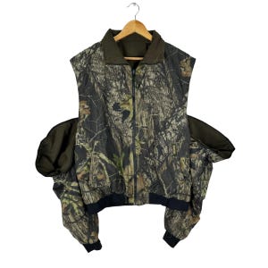 May include: A sleeveless camouflage jacket with a zip fastening and two attached sleeves. The jacket is made from a lightweight fabric and has a relaxed fit.