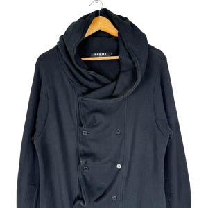 May include: Black hooded long-sleeved jacket with a double-breasted closure and a large, draped collar. The jacket has the word "Comme" printed on the label.