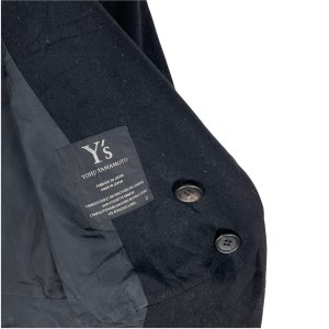 May include: Black Y's Yohji Yamamoto coat with a label that reads "Fabrique au Japon Made in Japan Composition et Instructions de Lavage Voir Etiquette Annexe Composition and Washing Instructions See Attached Label 2".