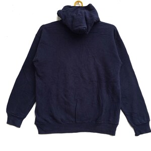 K&ouml;nnte beinhalten: Ein marineblauer Kapuzenpullover mit einer K&auml;ngurutasche. Der Pullover hat lange &Auml;rmel und einen gerippten Saum.