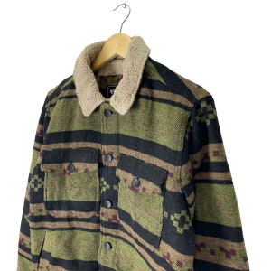 May include: A green, black and brown patterned flannel shirt with a brown sherpa collar. The shirt has a button-up front and two flap pockets.
