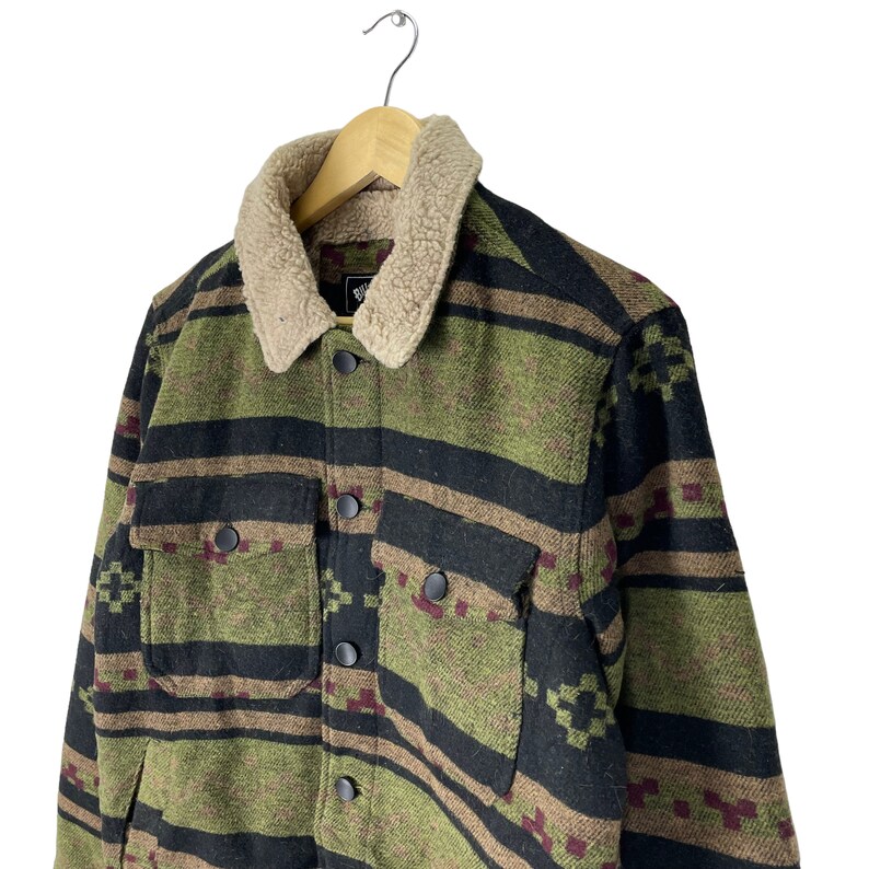 May include: A green, black and brown patterned flannel shirt with a brown sherpa collar. The shirt has a button-up front and two flap pockets.