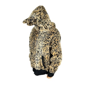 May include: A hooded jacket with a faux fur leopard print design. The jacket features a black bottom hem and cuffs, and a hood with a pointed shape. The fur is a mix of tan, brown, and black.