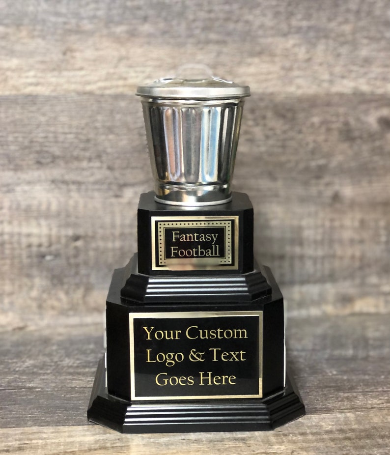 May include: A black and silver trophy with a trash can shaped top. The trophy has a black base with a silver plaque that says "Fantasy Football". The bottom plaque says "Your Custom Logo & Text Goes Here".