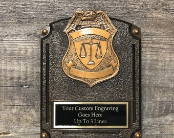 May include: A black and gold plaque with a raised eagle and scales of justice design. The plaque has a black rectangular plate with the text "Your Custom Engraving Goes Here Up To 3 Lines".