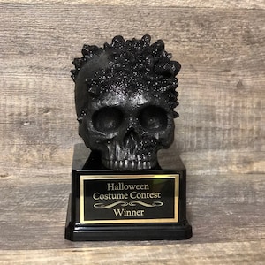 May include: Black skull trophy with a crystal-like texture on top, sitting on a black base with a gold plaque that reads "Halloween Costume Contest Winner".