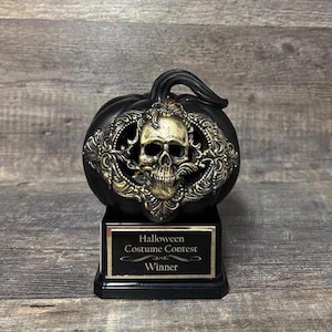 May include: Black and gold Halloween costume contest trophy shaped like a pumpkin with a skull design and the words "Halloween Costume Contest Winner" on the base.