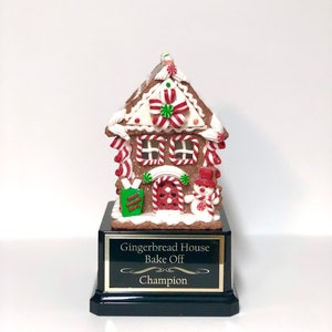 May include: A gingerbread house trophy with a black base and a gold plaque that reads "Gingerbread House Bake Off Champion".