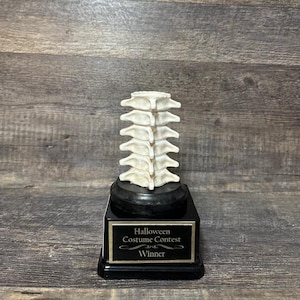 May include: A black and gold trophy with a white plastic spine model on top. The trophy base has the text "Halloween Costume Contest Winner".