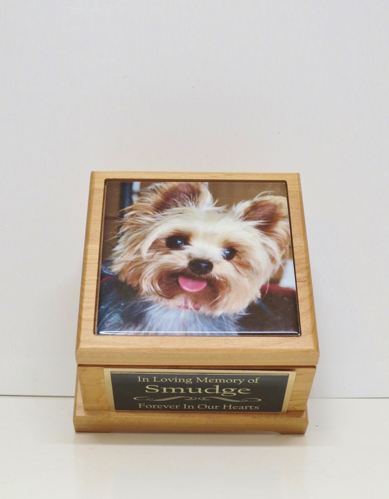 Puede incluir: Una urna de madera para mascotas con una foto de un Yorkshire Terrier en la parte delantera. La urna tiene una placa dorada que dice "In Loving Memory of Smudge Forever In Our Hearts".