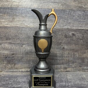 May include: A silver golf trophy with a gold golf ball design and a black base with a gold plaque that reads "Sunrise Golf Tournament Champion".
